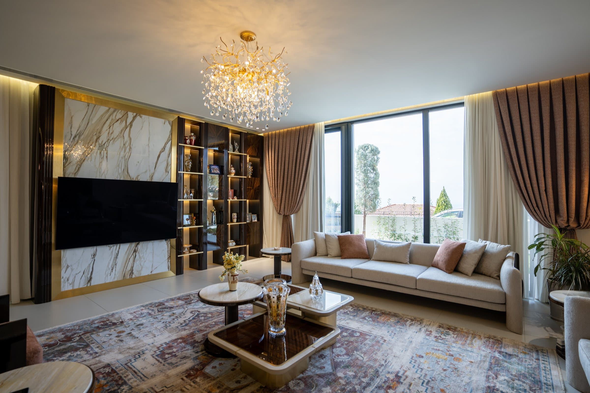 Living room with a marble and brass media wall, crystal chandelier and full-height glazing