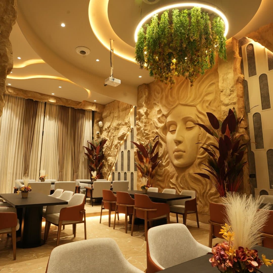Dining room facing a sculpted stone face, under a ring of hanging greenery